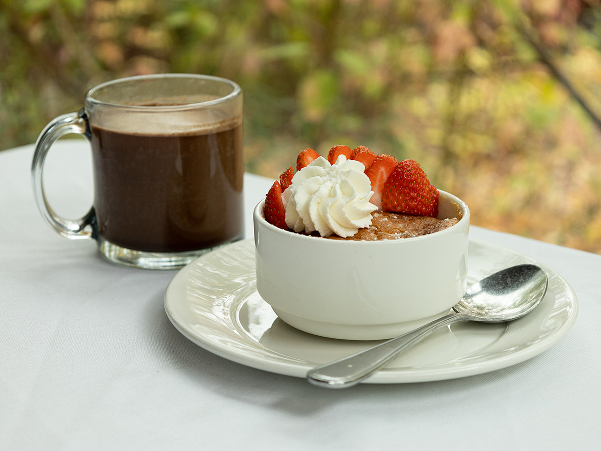 Lemon lava cake topped with whipped cream and strawberries, with a mug of hot chocolate